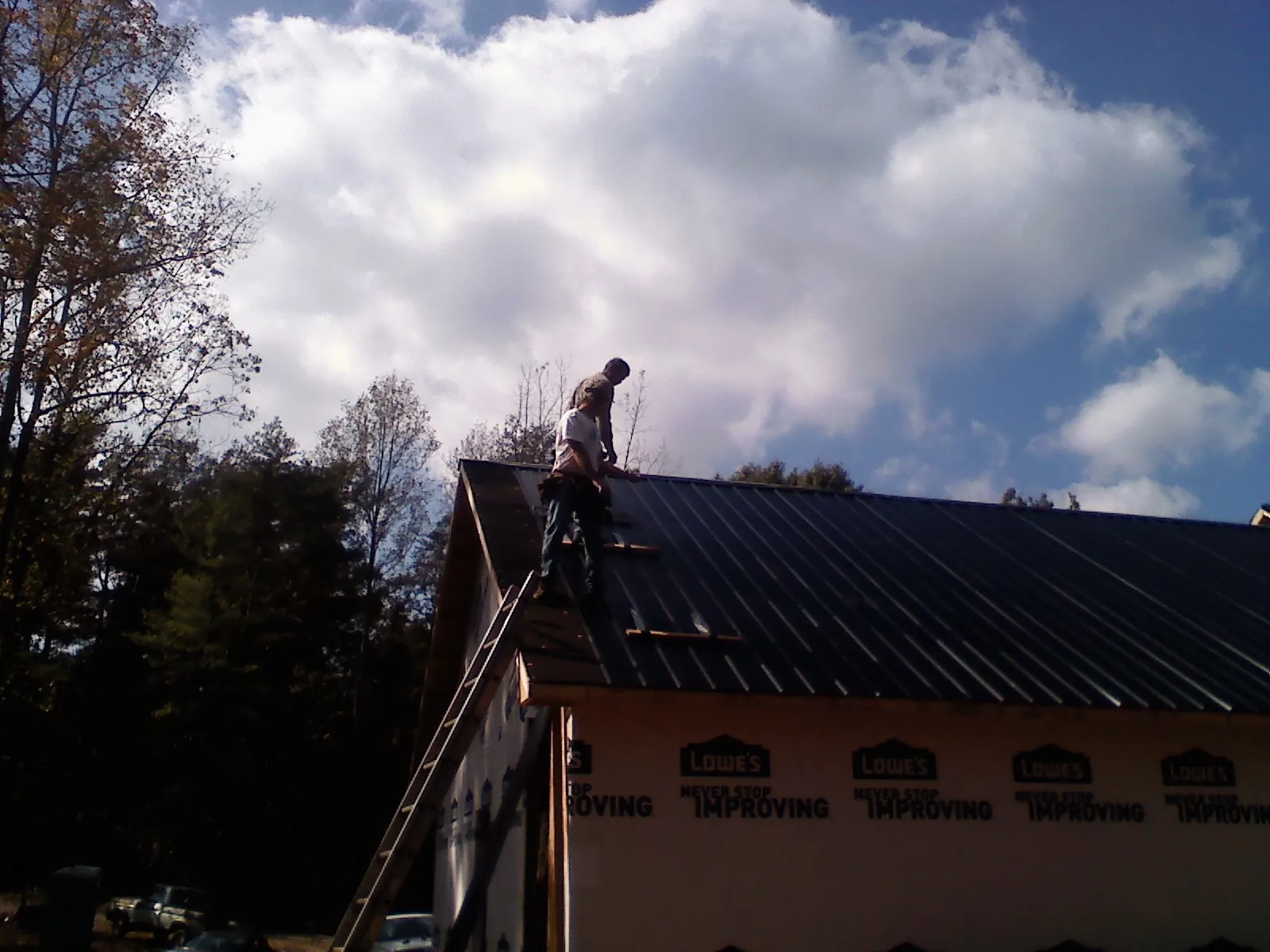 Roofer fastening dark metal panels high against a cloudy sky, from a Roof Inspection job in Bellefontaine